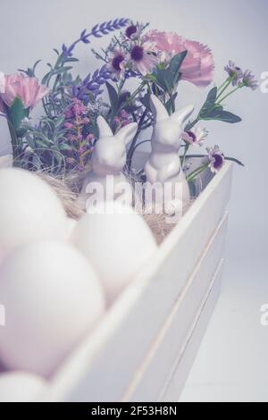 Coniglio di Pasqua in porcellana bianca con uova bianche e fiori scatola bianca in legno su sfondo bianco Foto Stock