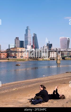Giovane coppia seduto sulla spiaggia di Bankside lungo il Tamigi A Londra durante il blocco all'inizio della primavera Foto Stock