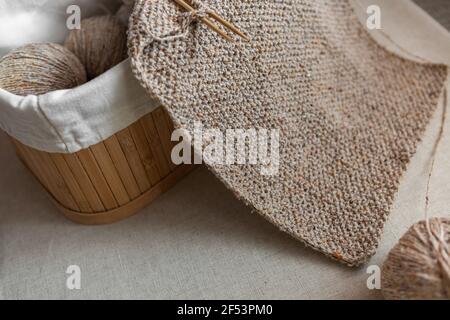 Primo piano di tessitura a maglia. Sciarpa di lana artigianale di colore sabbia e cesto con palle di filato. Messa a fuoco selettiva. Foto Stock