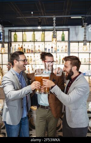 Giovani uomini d'affari bevono birra, parlano e sorridono mentre riposano al pub Foto Stock