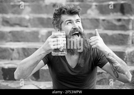 Uomo portatore felice che beve dopo una lunga giornata in ufficio. Allegro uomo tipsy tenere tazza di birra mentre mostra il pollice in su gesto, rilassarsi dopo il lavoro e. Foto Stock