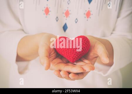 Le donne indossano una maglia a maglia che tiene a mano il cuore rosso. Concetto di amore, speranza, felice Valentino, sanità,donazione di organi,assicurazione, medico, Giornata del cuore del mondo, N. Foto Stock