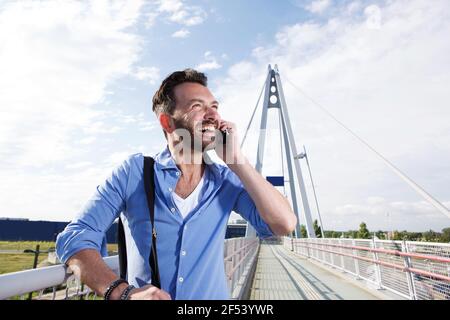 Ritratto di felice viaggiatore maschile in piedi sul ponte e parlare sul telefono cellulare Foto Stock