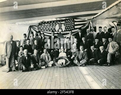 Formazione di gruppo con il Fest che sostiene il Signore sul ponte di decleveland contro la bandiera americana con emblema egiziano. Nel mezzo piccola ragazza con stile di vita (Cleveland intorno al mondo) e Fes con l'iscrizione Siria, accanto ad esso un Signore con Fes Salaam Foto Stock