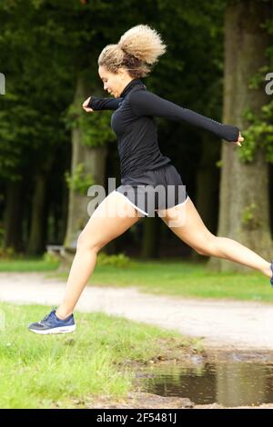 Ritratto di donna sportiva che salta sopra la puddle Foto Stock