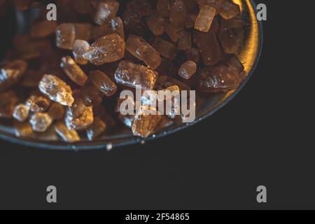 Zucchero barista di specialità di cristalli di demerara non raffinati su cucchiaio d'argento su sfondo scuro e umoroso. Primo piano Foto Stock