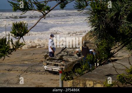 Gold Coast Australia. Soleggiato dopo una tempesta che causa danni lungo la costa. Uomini che ispezionano auto distrutte nel parcheggio sulla spiaggia. Foto Stock