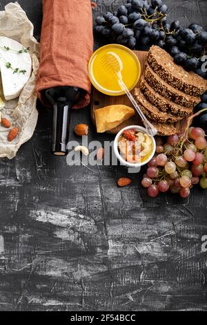 Cibo snack ingredienti formaggi diversi uve miele vino pane su fondo di cemento scuro. Composizione del vino e del formaggio. Cucina Mediterranea cibo Foto Stock