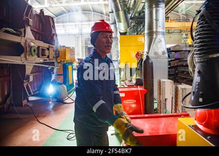 Ekibastuz, regione di Pavlodar, Kazakhstan-28 maggio 2012: Impianto di costruzione di automobili. Operaio asiatico e apparecchio rosso. Saldatrice sinistra. Foto Stock