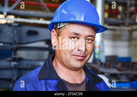 Ekibastuz, regione di Pavlodar, Kazakhstan - 28 maggio 2012: Impianto di carriage-building. Ritratto di operaio meccanico asiatico in casco da lavoro blu. Foto Stock