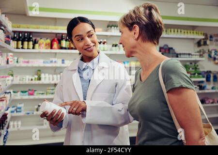 Felice farmacista che dà il flacone di medicinale alla cliente femminile in farmacia Foto Stock