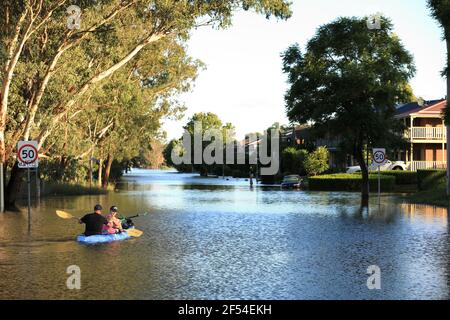 Un uomo e una donna in kayak che si addormentano su una strada allagata a McGraths Hill durante l'alluvione del fiume Hawkesbury-Nepean del marzo 2021, in Australia. Foto Stock