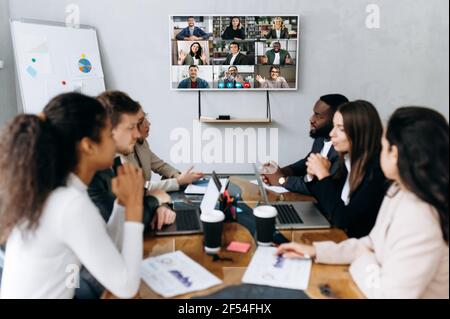 Colleghi multietnici di successo che hanno condotto negoziati in un ufficio moderno. Uomini d'affari in conferenza online che discutono di domande di lavoro, sviluppando una nuova strategia per l'azienda, briefing online Foto Stock