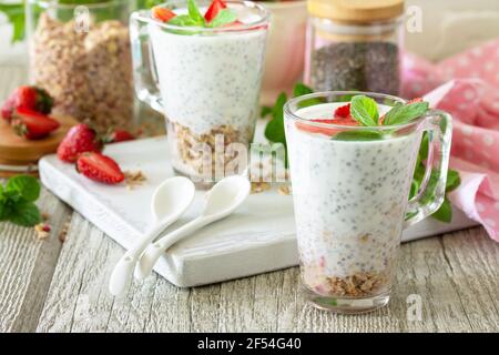 Colazione sana. Granola fatta in casa con fragola, yogurt, semi di chia, muesli fatti in casa e frutti di bosco freschi su un tavolo di legno. Foto Stock