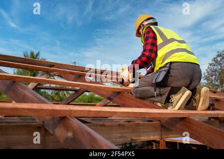 Tetto asiatico che lavora sulla struttura del tetto di costruzione in cantiere, Roofer utilizzando aria o pistola pneumatica per unghie e l'installazione su struttura del tetto in legno Foto Stock