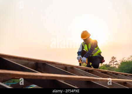 Tetto asiatico che lavora sulla struttura del tetto di costruzione in cantiere, Roofer utilizzando aria o pistola pneumatica per unghie e l'installazione su struttura del tetto in legno Foto Stock