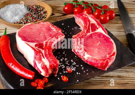 Due costolette fresche crude su tavola di legno su sfondo di legno con sale e pepe in stile rustico Foto Stock