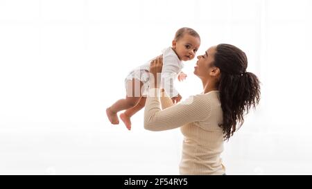 Bimbo con mummia africana che trasporta il bambino giocando con il neonato, sfondo bianco Foto Stock