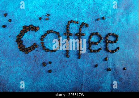 La parola caffè è scritta in chicchi di caffè su una superficie di tessuto turchese e blu brillante. Foto orizzontale. Foto Stock