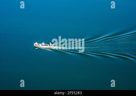 La barca da pesca bianca con tre persone a bordo galleggia in un lago. Foto Stock