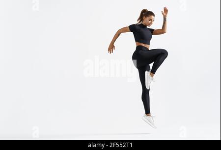 Donna in forma che si esercita all'interno. Atleta giovane sana che fa l'allenamento di idoneità. Sportivo in abbigliamento sportivo saltando su sfondo bianco, allenamento Foto Stock