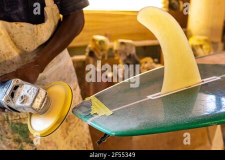 Primo piano di un artigiano africano tavola da surf Shaper lavorare in un'officina di riparazione Foto Stock