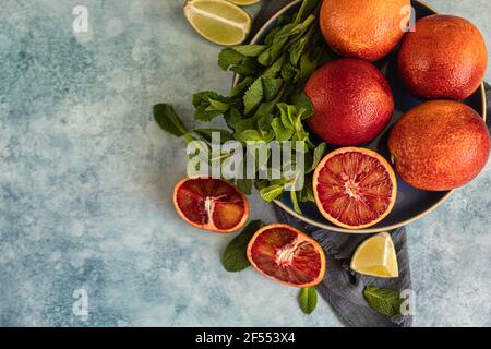 Arance siciliane rosse con lime e menta su sfondo blu. Agrumi interi e tagliati a fette. Vista dall'alto. Messa a fuoco selettiva. Foto Stock