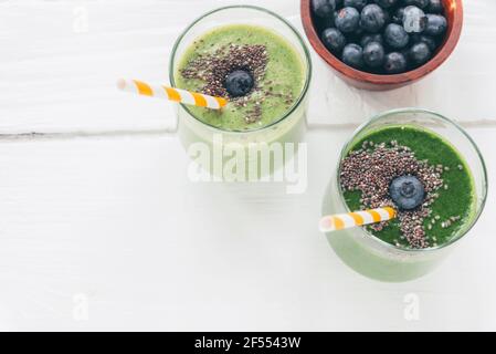Due frullati verdi in bicchieri con cannucce e mirtilli in un recipiente. Concetto di cibo sano. Vista dall'alto, disposizione piatta, spazio per la copia. Foto Stock