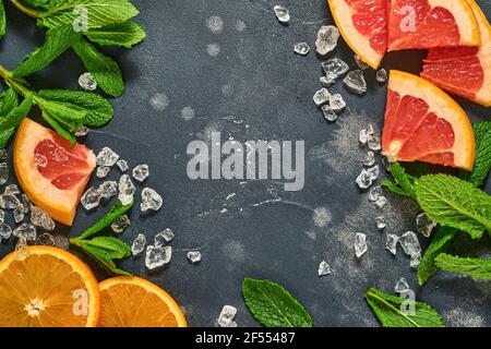 Fette di pompelmo e arancia, menta, zucchero di canna, ghiaccio, cocktail tubes, centrifuga o spremiagrumi su fondo nero vecchio di pietra. Ingredienti per fare estate b Foto Stock