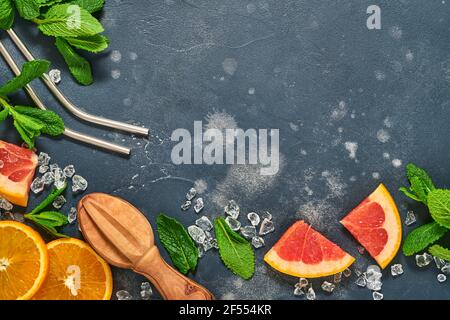 Fette di pompelmo e arancia, menta, zucchero di canna, ghiaccio, cocktail tubes, centrifuga o spremiagrumi su fondo nero vecchio di pietra. Ingredienti per fare estate b Foto Stock