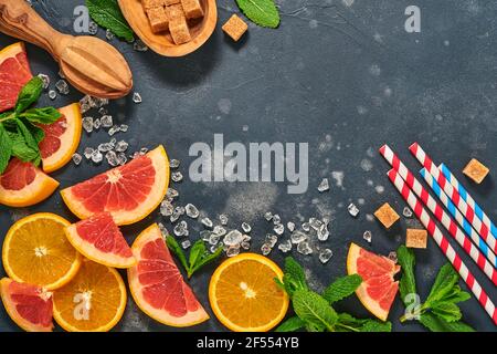 Fette di pompelmo e arancia, menta, zucchero di canna, ghiaccio, cocktail tubes, centrifuga o spremiagrumi su fondo nero vecchio di pietra. Ingredienti per fare estate b Foto Stock