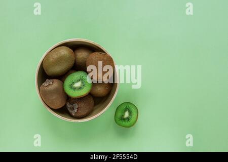 Frutta kiwi in una ciotola su sfondo verde. Cibo vegano sano. Vista dall'alto, disposizione piatta, spazio per la copia. Foto Stock