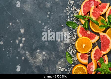 Fette di pompelmo e arancia, menta, zucchero di canna, ghiaccio, cocktail tubes, centrifuga o spremiagrumi su fondo nero vecchio di pietra. Ingredienti per fare estate b Foto Stock