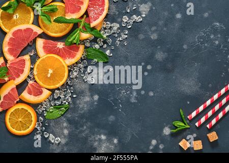 Fette di pompelmo e arancia, menta, zucchero di canna, ghiaccio, cocktail tubes, centrifuga o spremiagrumi su fondo nero vecchio di pietra. Ingredienti per fare estate b Foto Stock
