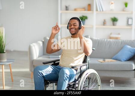 Ragazzo nero con handicap positivo in sedia a rotelle che ascolta la musica con gli occhi chiusi, utilizzando le cuffie a casa Foto Stock