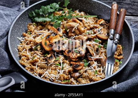 classico risotto cremoso ai funghi cosparso di parmigiano grattugiato in una padella, primo piano, cucina italiana Foto Stock