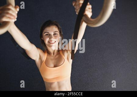 Vista ad alto angolo sportivo felice motivata in Activewear reggiseno appeso su circoli di ginnastica crossfit, fotocamera sorridente godere di allenamento, come sfida Foto Stock