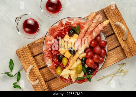 Piatto di antipasti italiani con prosciutto, grissini, uva, olive e formaggio su vassoio di legno. Vista dall'alto Foto Stock