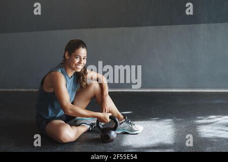 Concetto di salute, motivazione e palestra. Allenatore sportivo fitness prendere cura dei muscoli, riposare dopo le squadre crossfit, tenere kettlebell, sedersi piano del club benessere Foto Stock