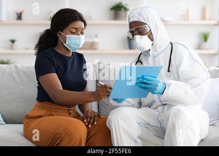 Donna afroamericana in maschera di faccia che firma le carte mediche Foto Stock