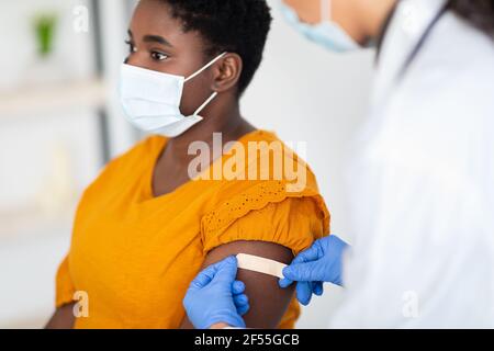 Donna che ottiene vaccinato mentre medico che applica il Plaster dopo l'iniezione all'interno Foto Stock