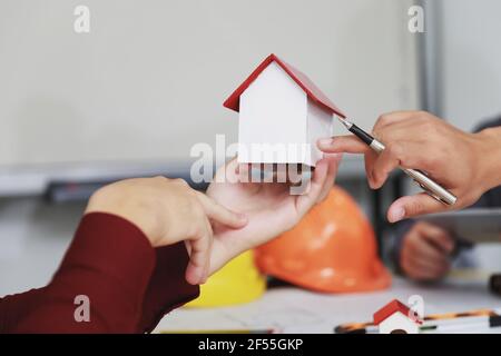Modello di casa a disposizione su un team fiducioso di architetti che lavorano insieme in un ufficio. Affari, architettura, costruzione di edifici e conca immobiliare Foto Stock