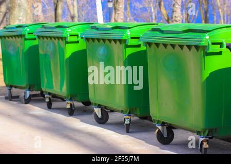Grandi bidoni di plastica verde sulla strada della città. Contenitori su ruote con maniglia per raccogliere rifiuti commerciali e residenti. Smaltimento della famiglia e. Foto Stock