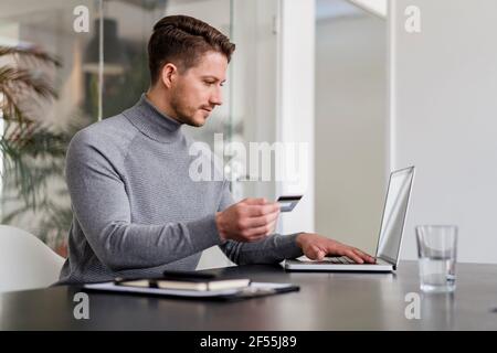 Uomo d'affari che paga online con carta di credito su computer portatile in ufficio Foto Stock