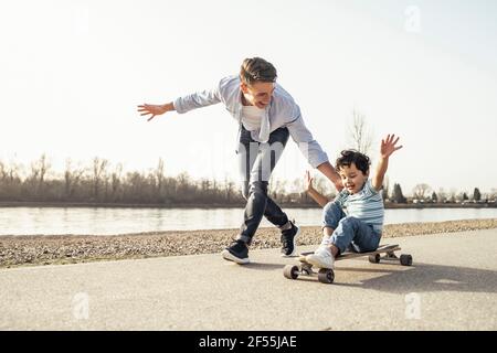 Giovane uomo che gioca con seduto sullo skateboard durante la giornata di sole Foto Stock