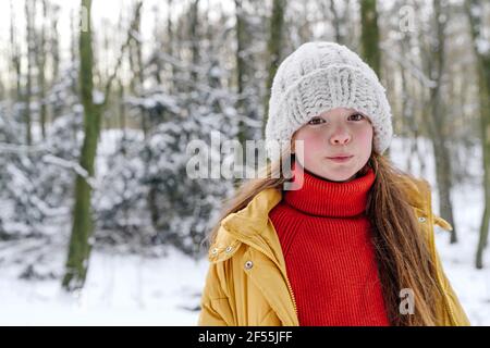 Ragazza che indossa cappello a maglia in piedi contro gli alberi durante la neve Foto Stock