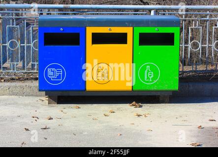 Tre bidoni di riciclaggio blu, verde e giallo in metallo in ambiente urbano. Contenitori per diversi tipi di rifiuti. Smistamento rifiuti separato per vetro, plastica, Foto Stock