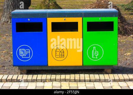 Tre bidoni di riciclaggio blu, verde e giallo in metallo in ambiente urbano. Contenitori per diversi tipi di rifiuti. Smistamento rifiuti separato per vetro, plastica, Foto Stock