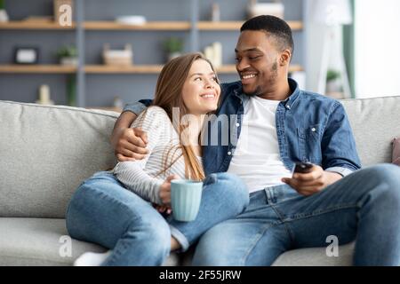 Felice coppia interracial amorevole rilassarsi a casa, guardare la tv e bere caffè Foto Stock