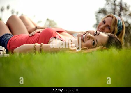 Bella donna allegra con amica femminile sdraiata sull'erba dentro parcheggio Foto Stock